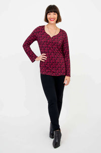 Full length image of a woman in magenta and black patterned long sleeve top and black pants