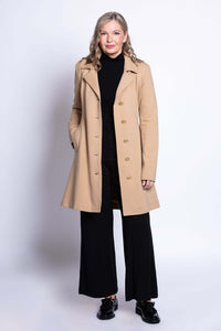 Full body of woman in tan modal trench jacket, black outfit, and black shoes