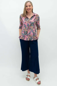 Full-body view of woman in pink paisley blouse and navy pants, front-facing, hands in pockets