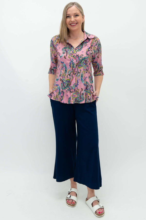 Full-body view of woman in pink paisley blouse and navy pants, front-facing, hands in pockets