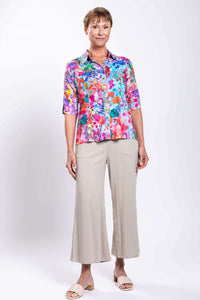 Full body view of woman in a vibrant floral button-up blouse paired with beige pants
