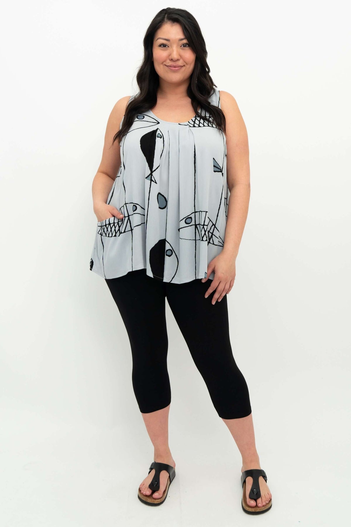 Model in full view wearing light blue pleated tank top with fish print, black leggings, and sandals
