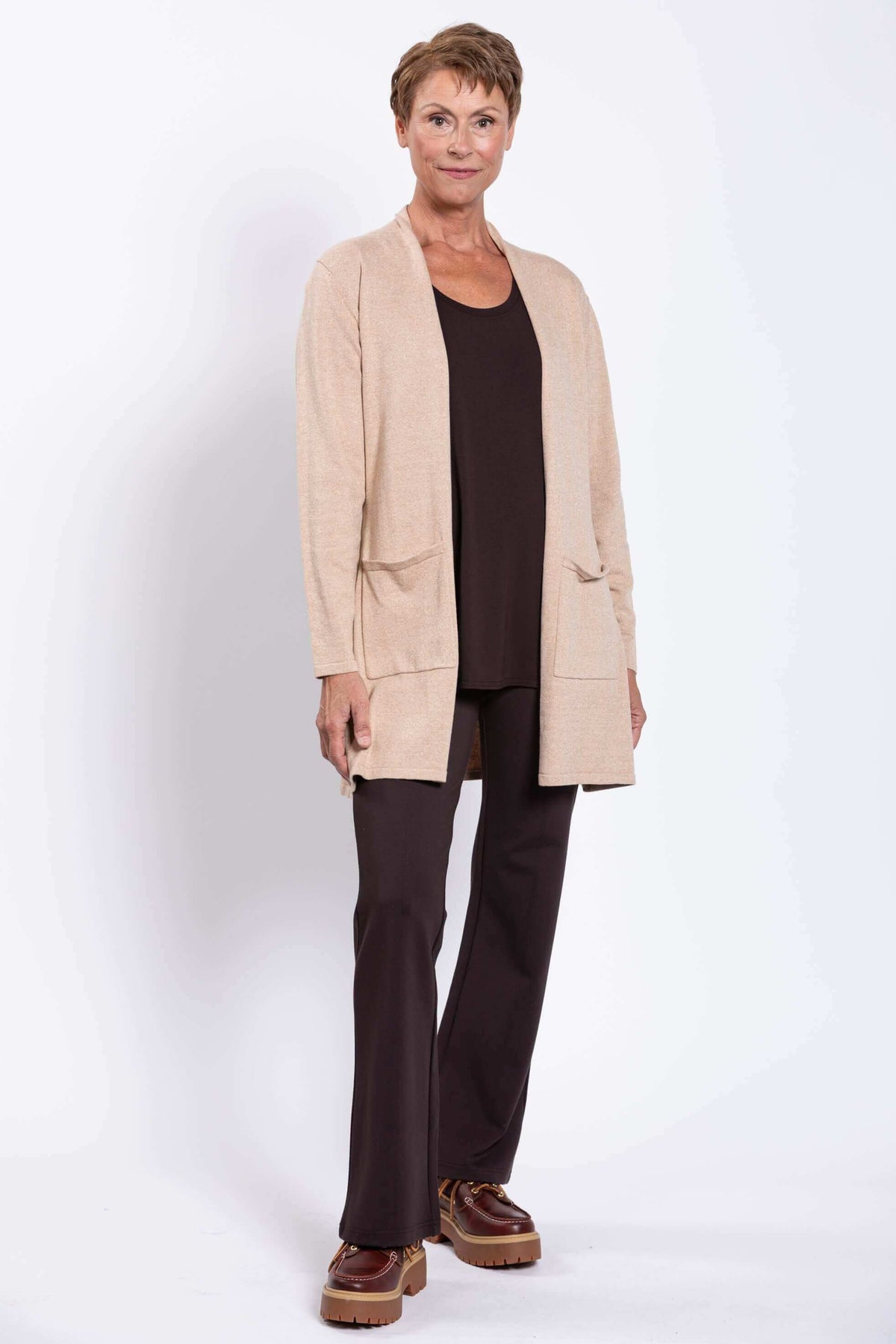 Full-body view of a woman modeling a beige cardigan with patch pockets and brown trousers