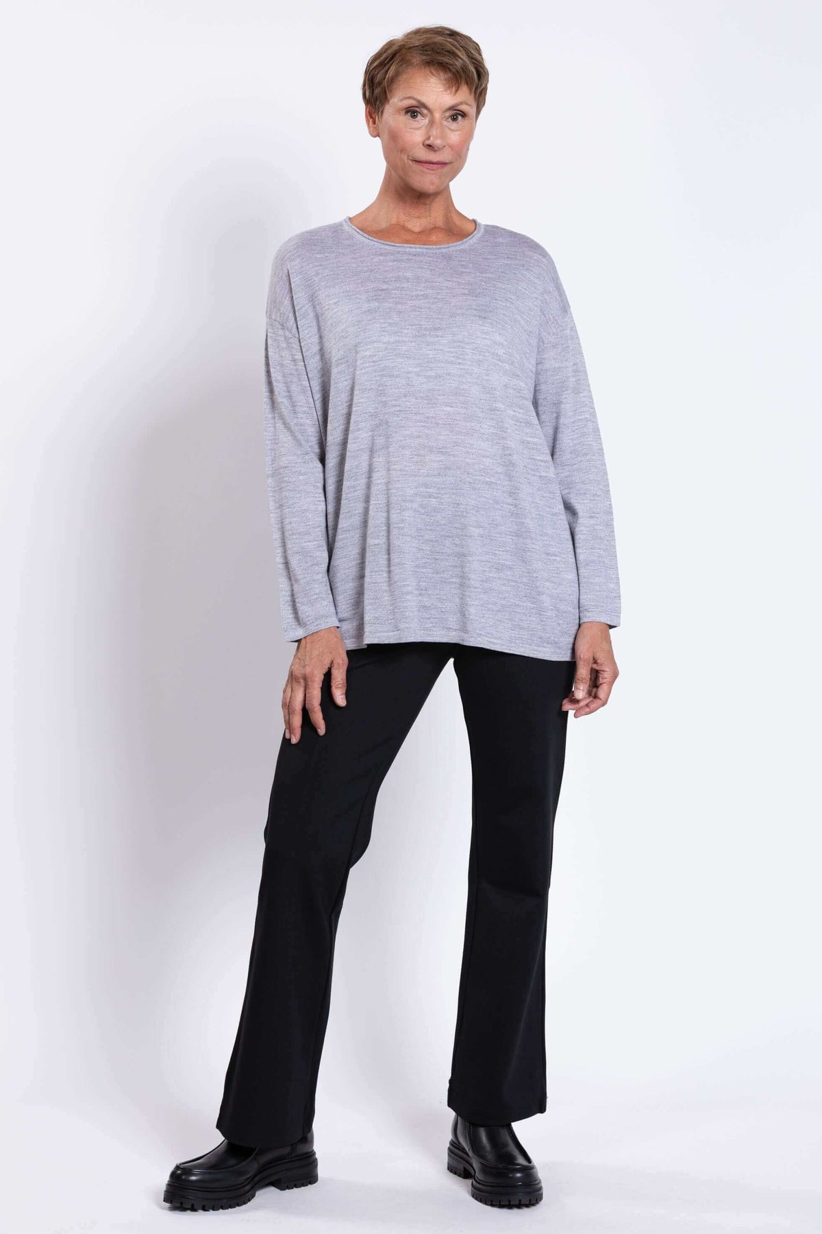 Full body view of woman modeling a light grey Merino wool sweater with black pants