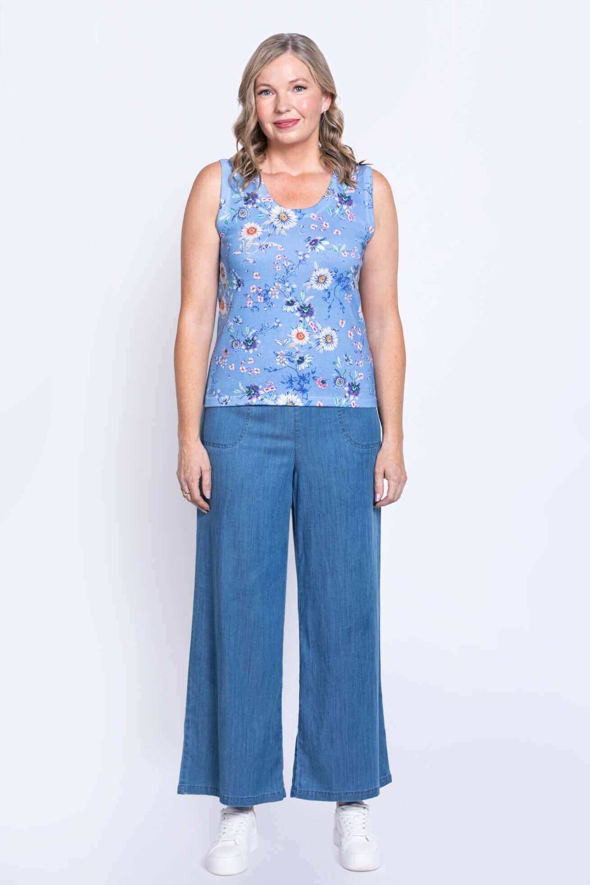 Full view of woman in blue floral tank top and wide-leg jeans, facing forward