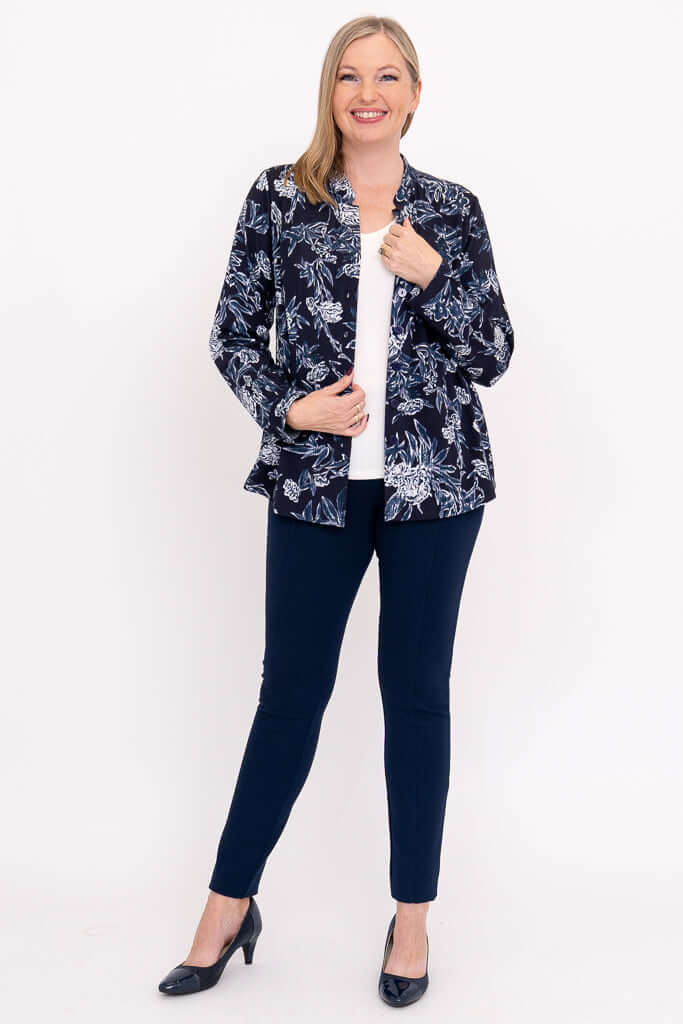 Full body view of model in navy floral top, open over a white shirt and navy pants