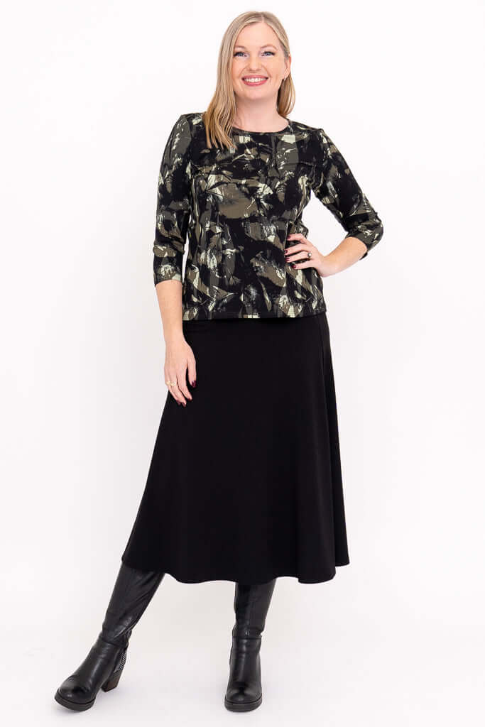 Full outfit view of woman in olive and black print tee with black skirt and boots