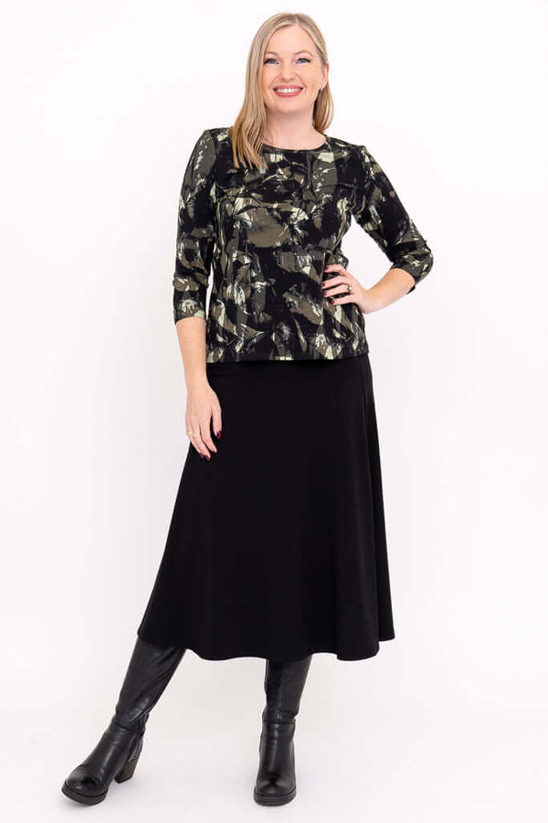 Full outfit view of woman in olive and black print tee with black skirt and boots