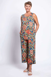 Woman in full floral peony print outfit, smiling, showing sleeveless top and pants, hands in pockets