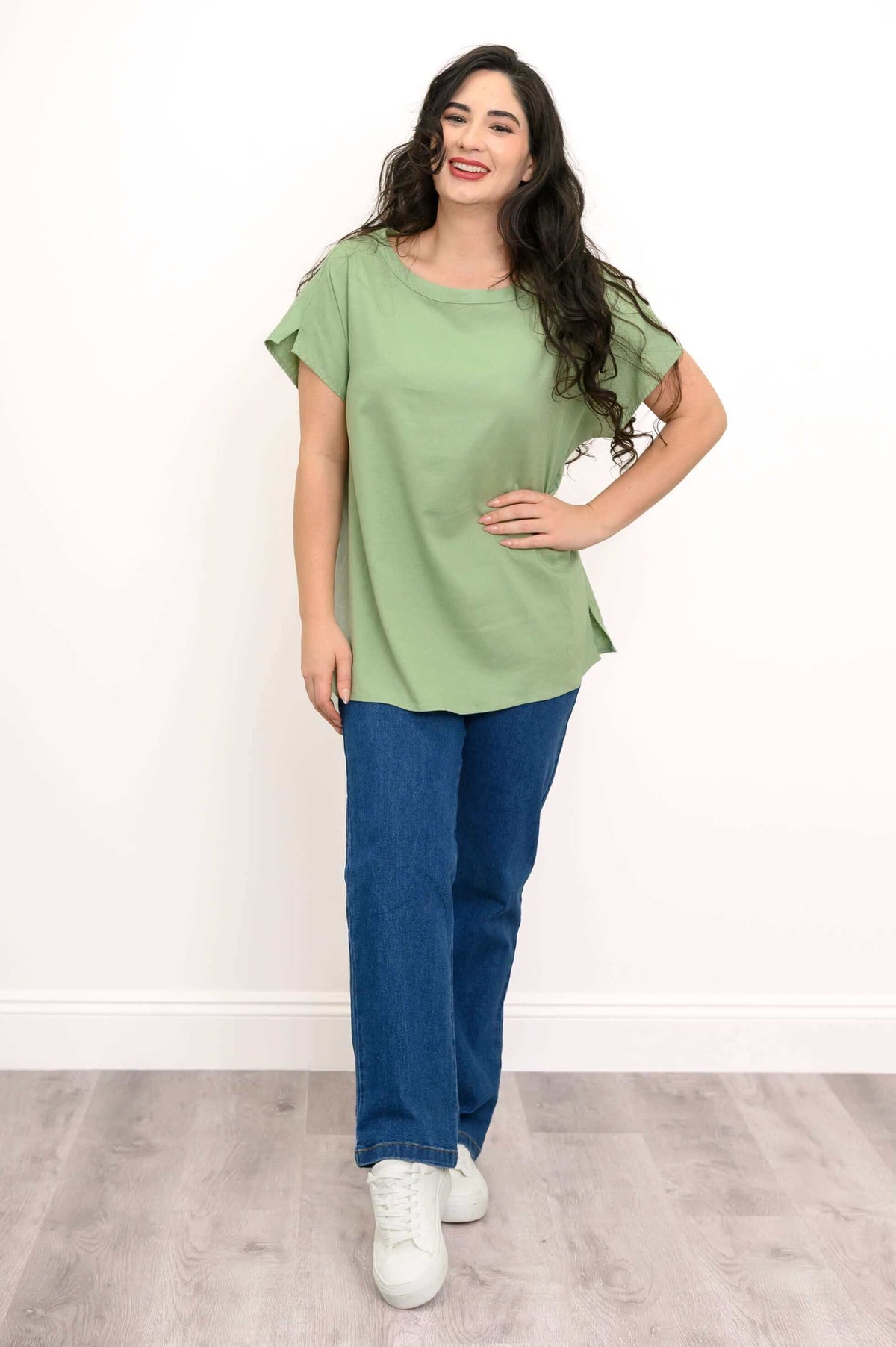 Full view of a woman in a sage green relaxed fit tee paired with blue jeans and white sneakers