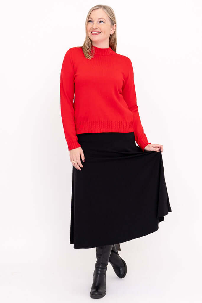 Woman in red mock neck sweater and black skirt posing, showing full outfit and boots