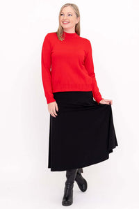 Woman in red mock neck sweater and black skirt posing, showing full outfit and boots