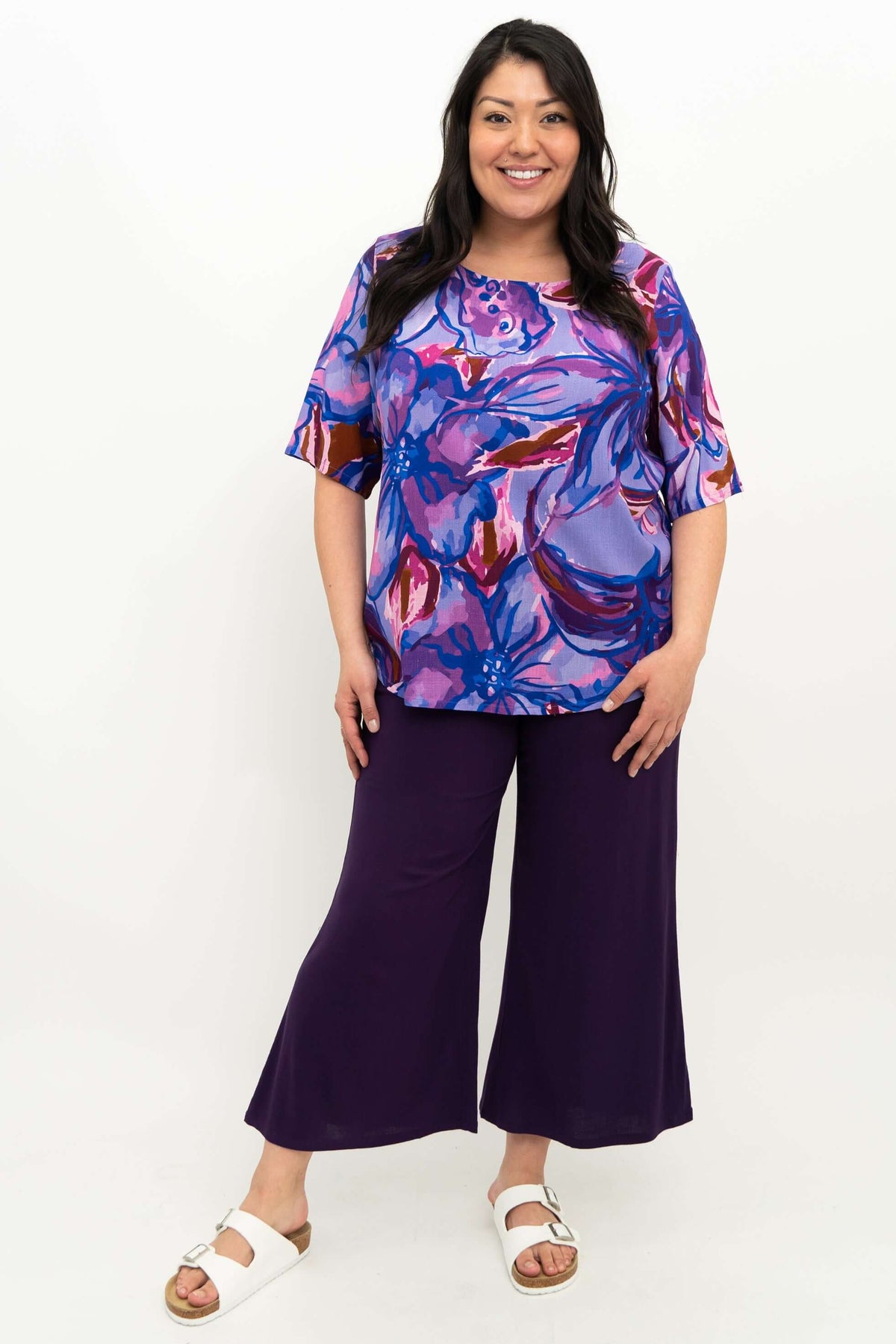 Woman standing in full outfit featuring purple floral blouse and wide-leg pants