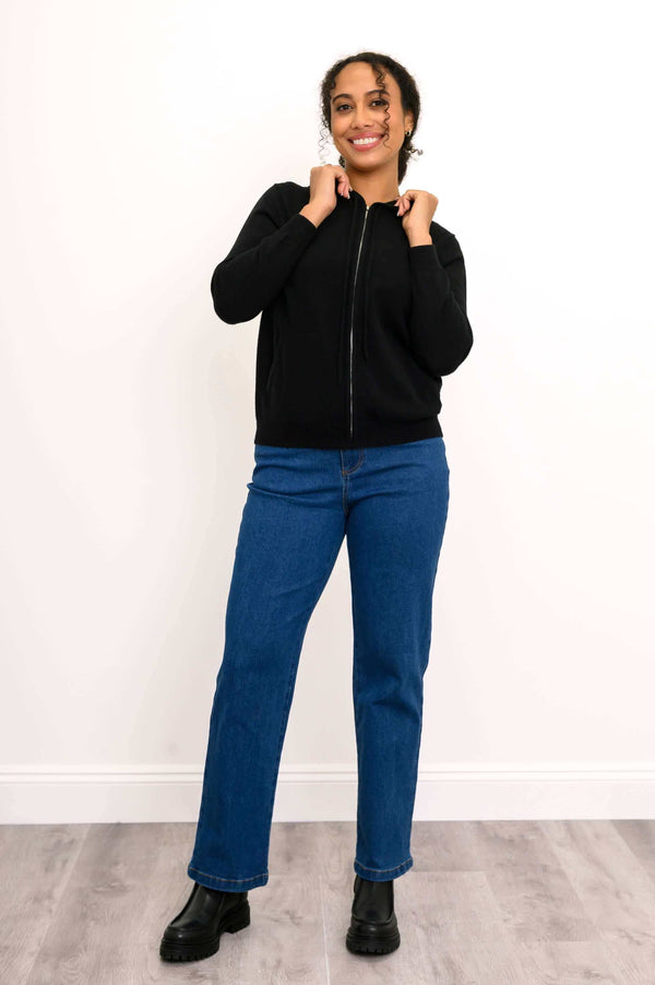 Full-body view of woman wearing black zip-up hoodie, jeans, and boots