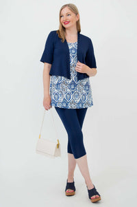 Woman in a blue mosaic tank top with navy cropped jacket, leggings, and white purse