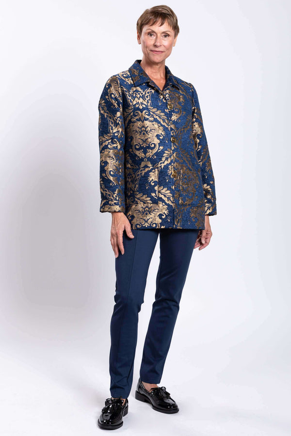Full body view of a woman in a blue and gold patterned jacquard coat and navy pants