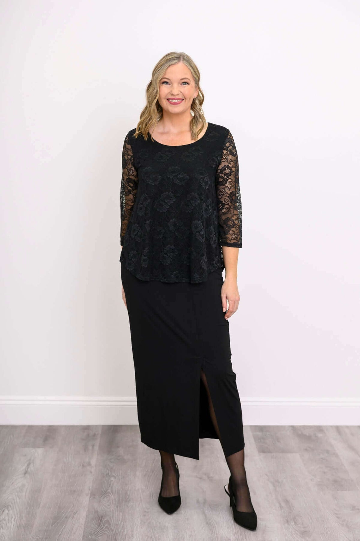 Woman in black lace top and long black skirt standing in bright room