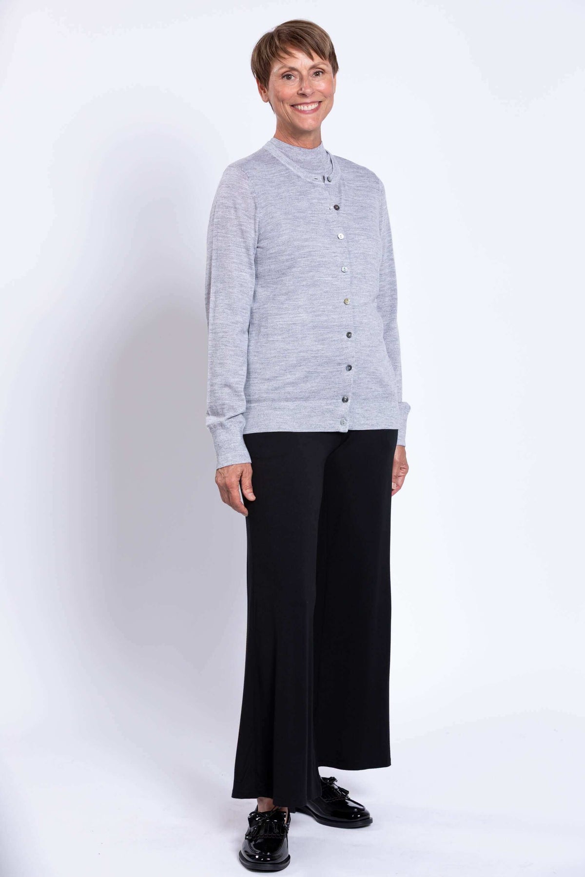 Woman standing in a light grey merino wool cardigan, black pants, and black loafers