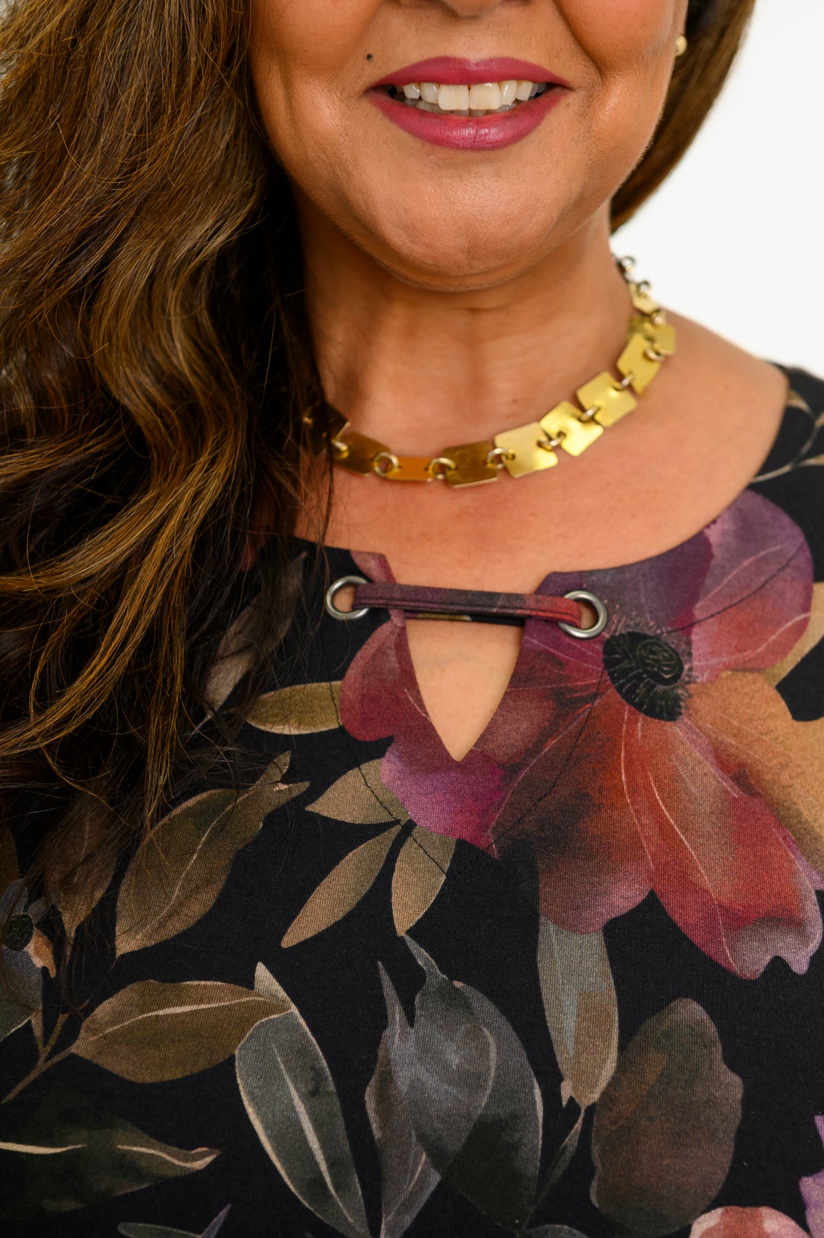 Close-up of a women's colorful floral knit top, highlighting the notched keyhole neckline and gold necklace.