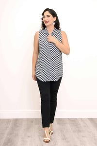Woman in a gingham tank top and black pants, standing with hand near collar