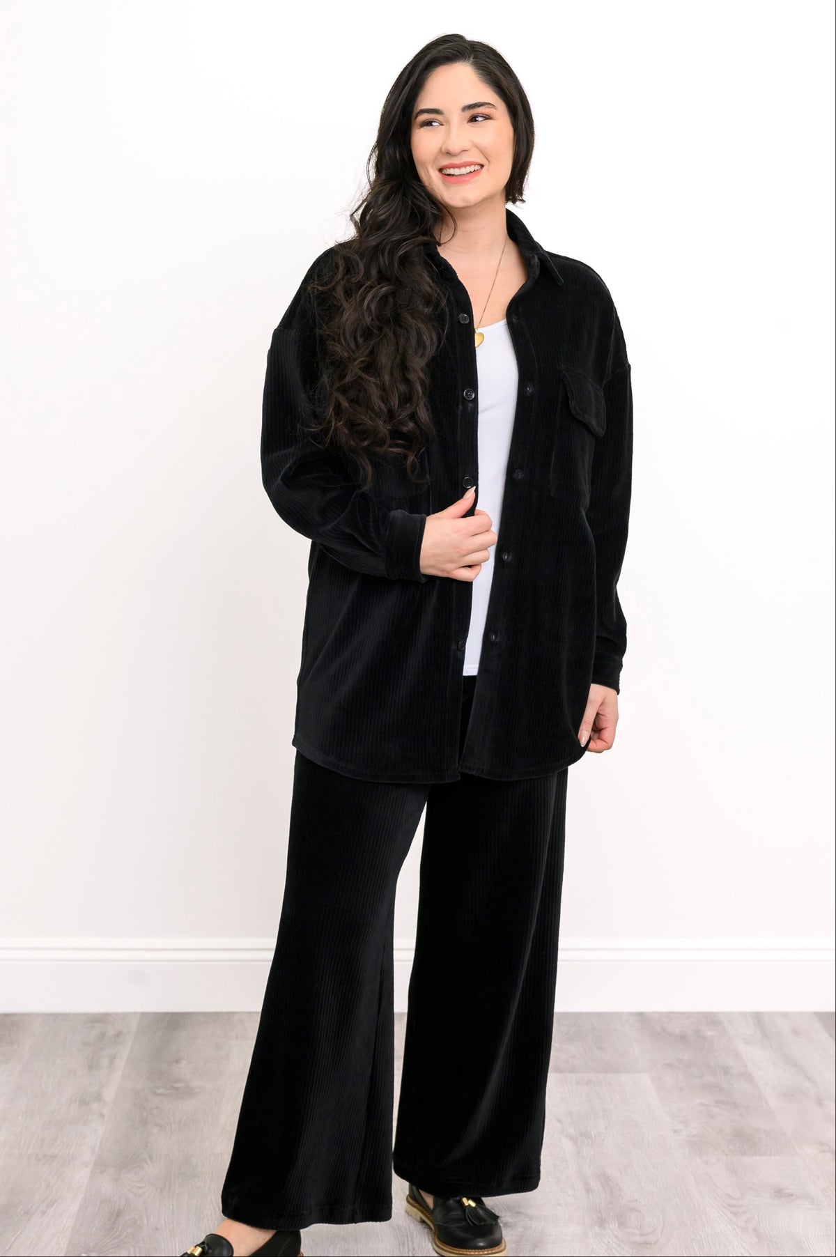Smiling woman wearing an open black corduroy button-down shirt jacket with matching wide-leg trousers