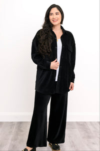 Smiling woman wearing an open black corduroy button-down shirt jacket with matching wide-leg trousers