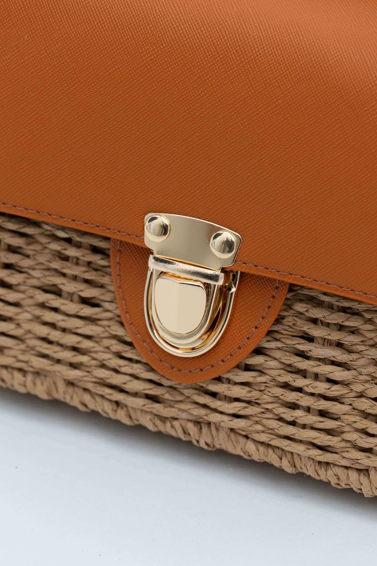 Close-up of gold clasp on rattan crossbody bag with brown faux leather flap