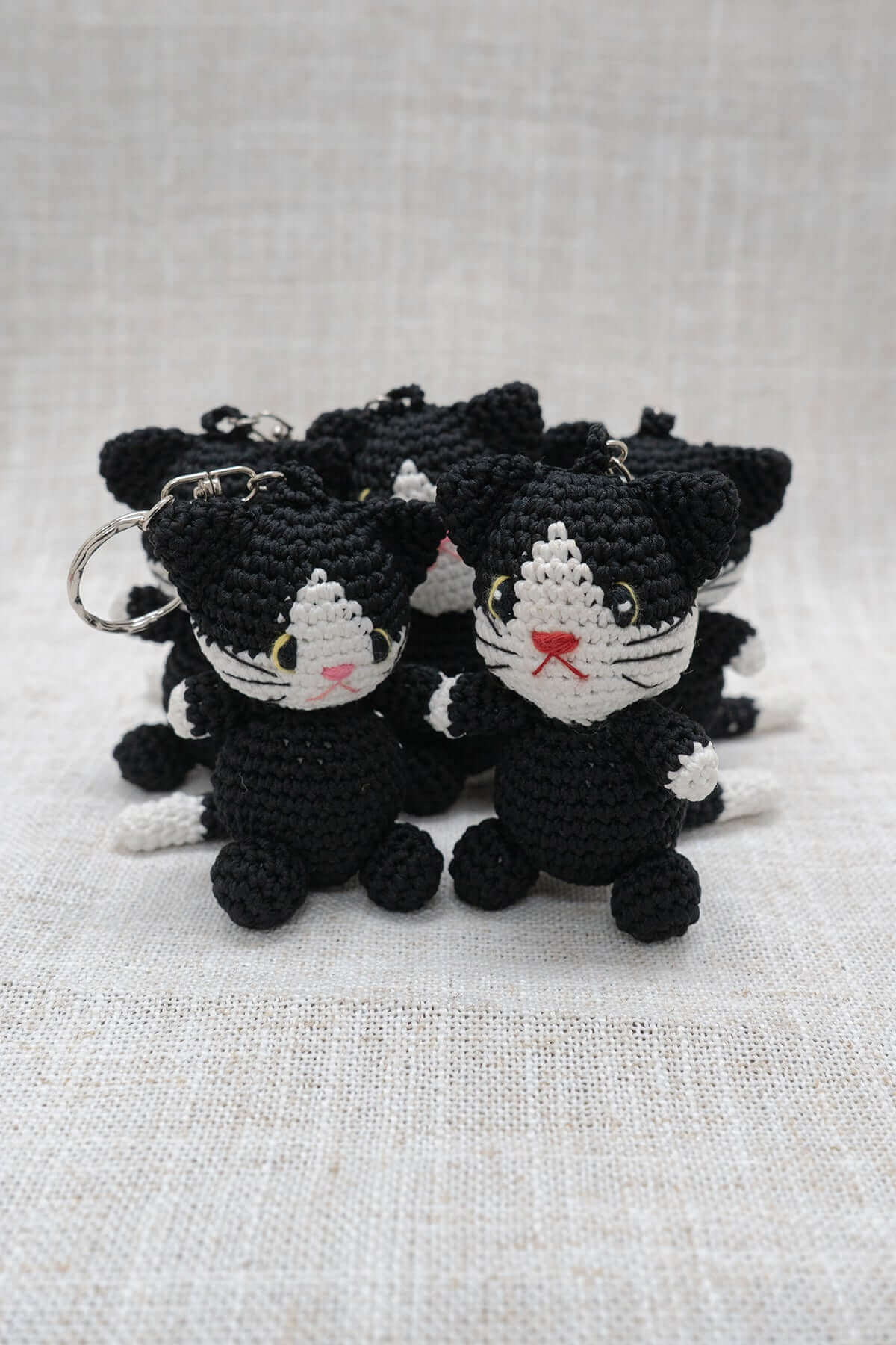 Hand-crocheted black and white cat keychains arranged together on a light cloth background