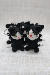Hand-crocheted black and white cat keychains arranged together on a light cloth background