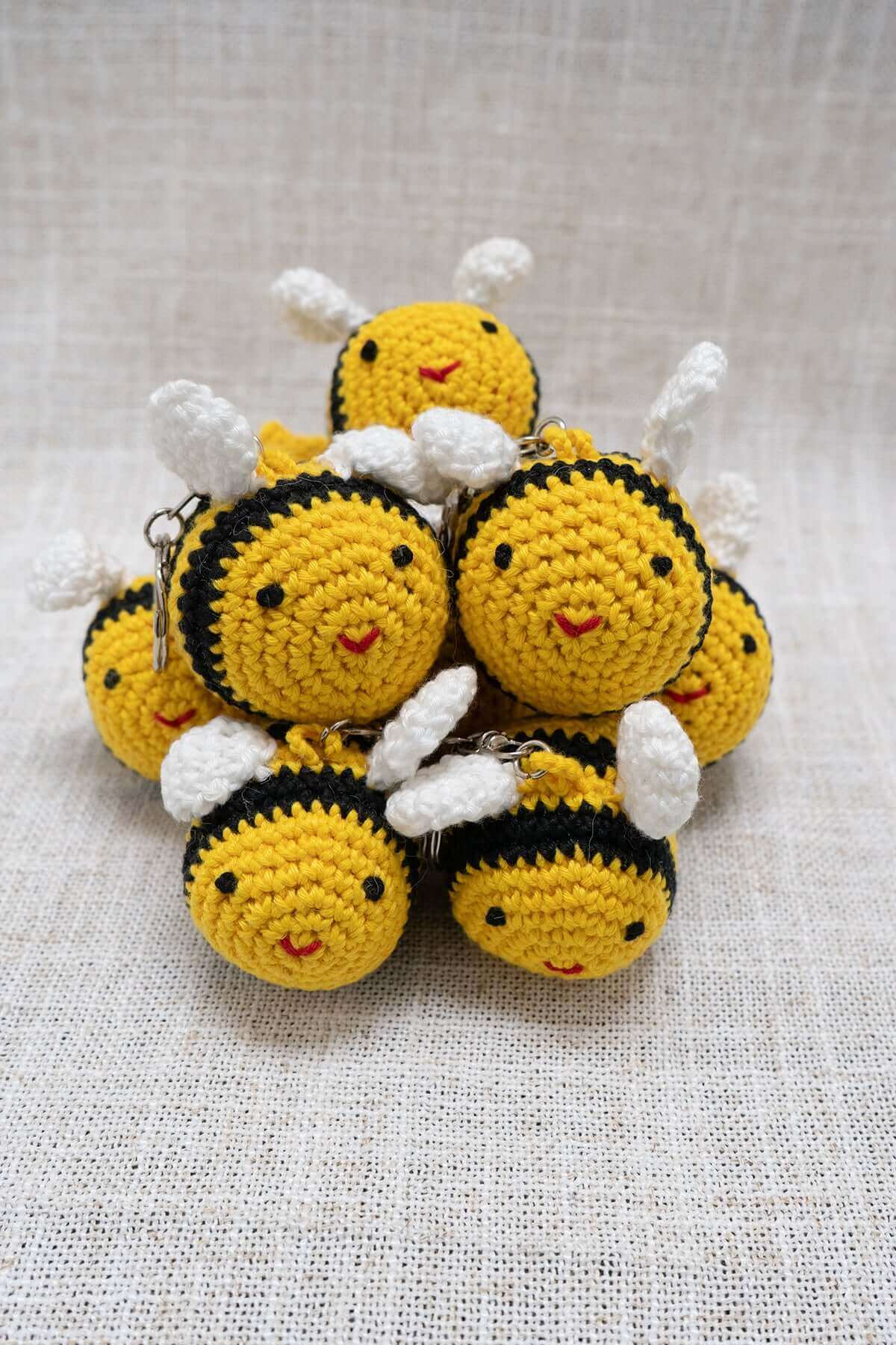A group of handmade crochet bee keychains with yellow, black, and white yarn, smiling faces, and small wings.