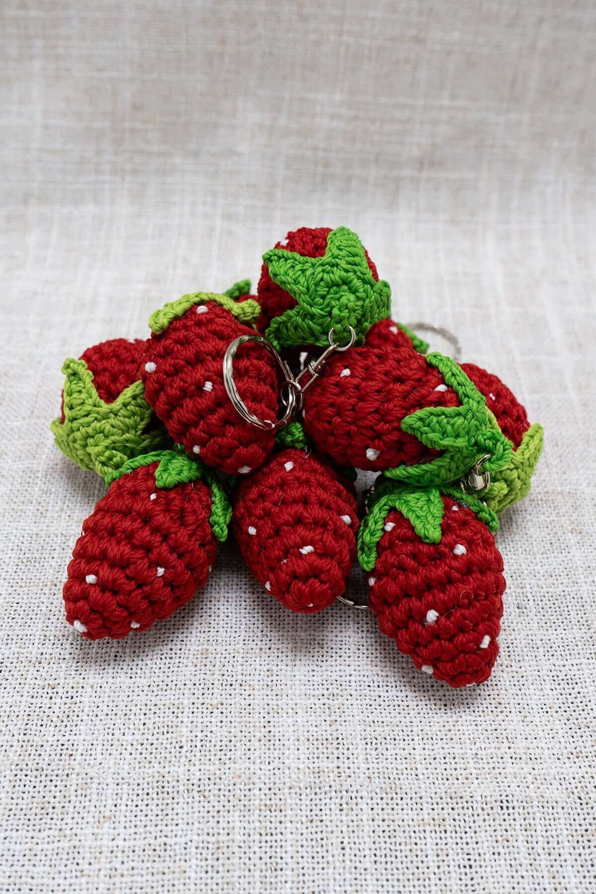 Handmade strawberry crochet keychains with green leaves arranged on a fabric surface