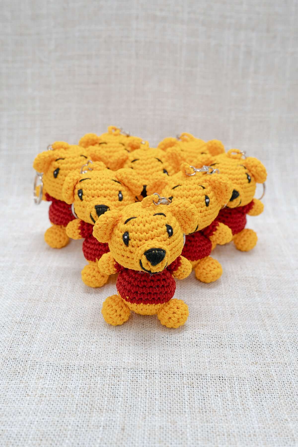 Handmade crochet bear keychains arranged in a group on a light fabric background