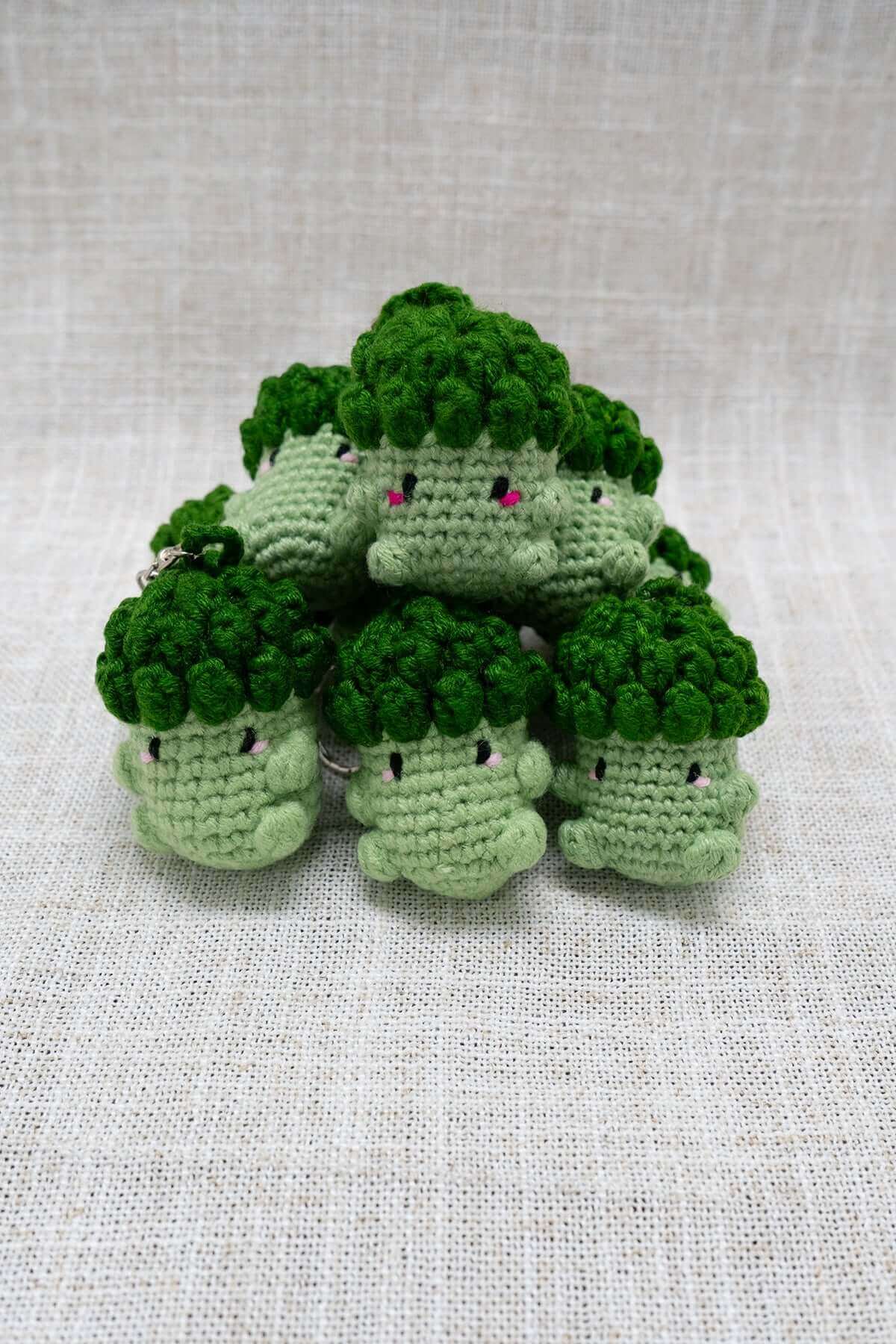 Group of handmade crochet broccoli keychains with cute faces stacked on fabric