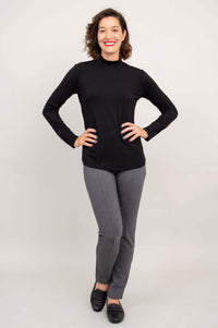 Woman posing with hands on hips, wearing a black mock neck top and gray pants