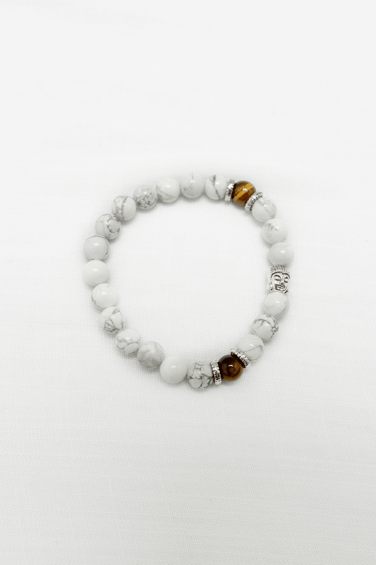 White howlite and tiger's eye beaded bracelet with silver Buddha charm on white fabric