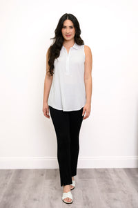 full body view of woman modeling a white sleeveless top, black pants, and white sandals