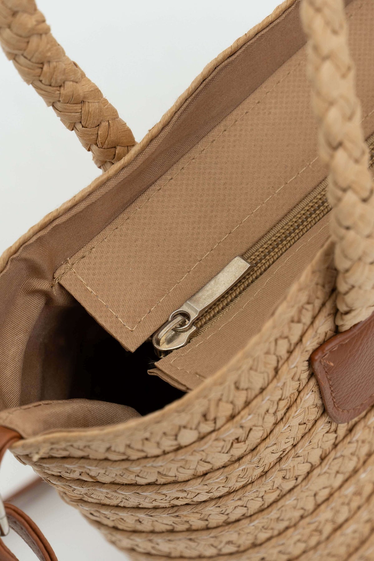 Close-up of interior zippered pocket inside the woven straw tote bag