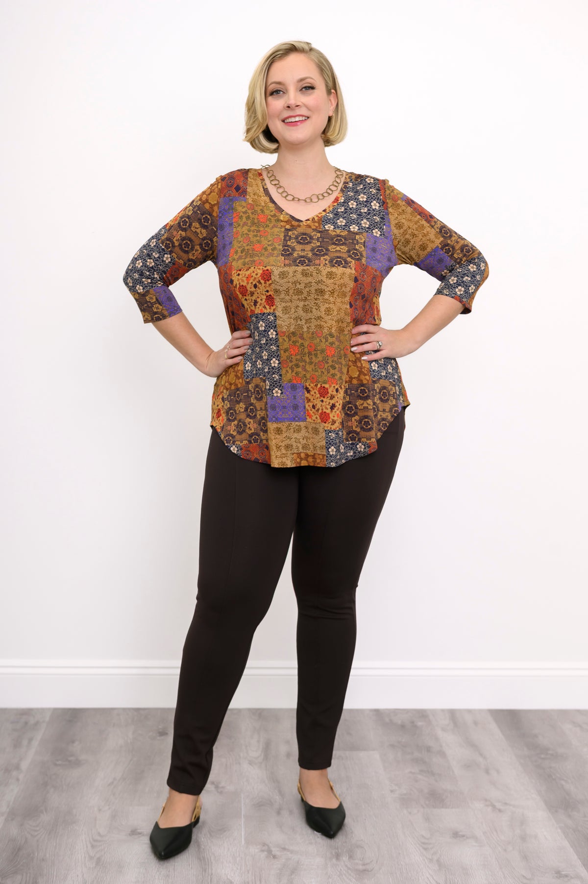 Model wearing a yellow and brown patterned V-neck bamboo tunic and brown pants, standing against a white wall.