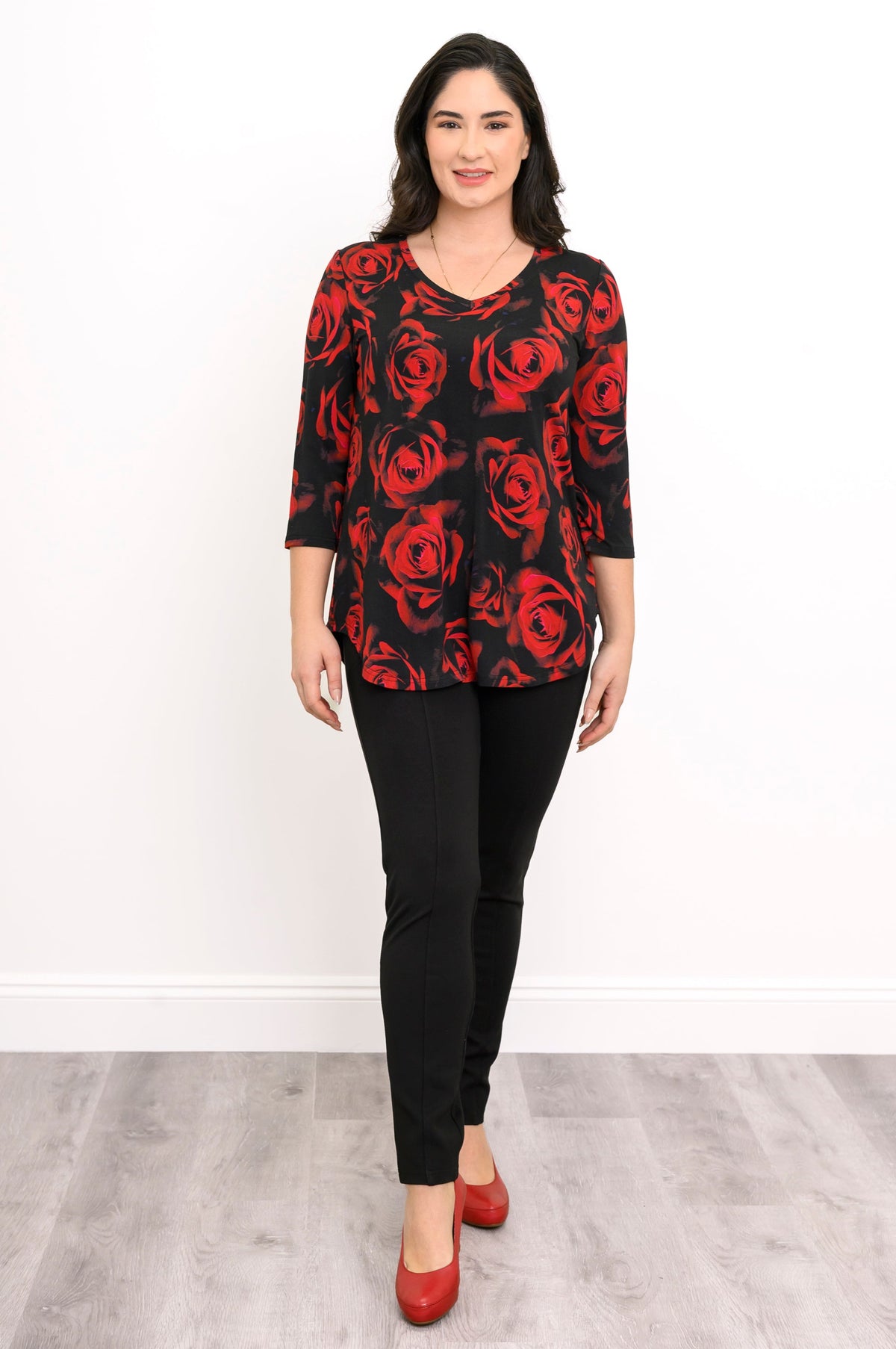 Front view of a female model wearing a bamboo top with 3/4 sleeves and a crimson floral design, with black pants and red heels, against a white backdrop and grey floor