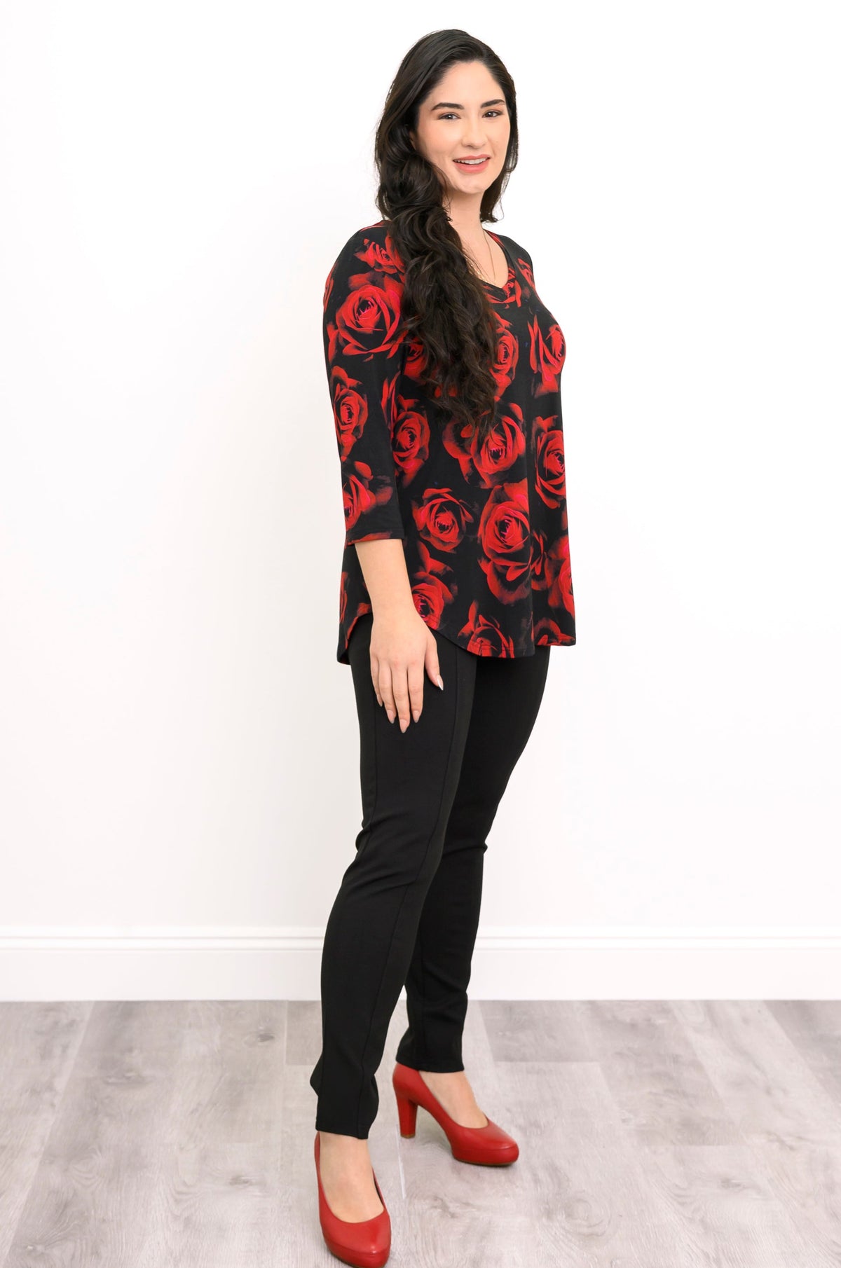 Side-facing front view of a female model wearing a bamboo top with casual 3/4 sleeves and a crimson floral design, with black pants and red heels, against a white backdrop and grey floor