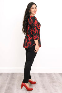 Side view of a female model wearing a bamboo top with casual 3/4 sleeves and a crimson floral design, with black pants and red heels, against a white backdrop and grey floor