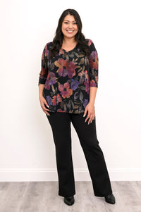Plus-size model in a dark pink floral knit tunic and black trousers, standing against a plain white wall.
