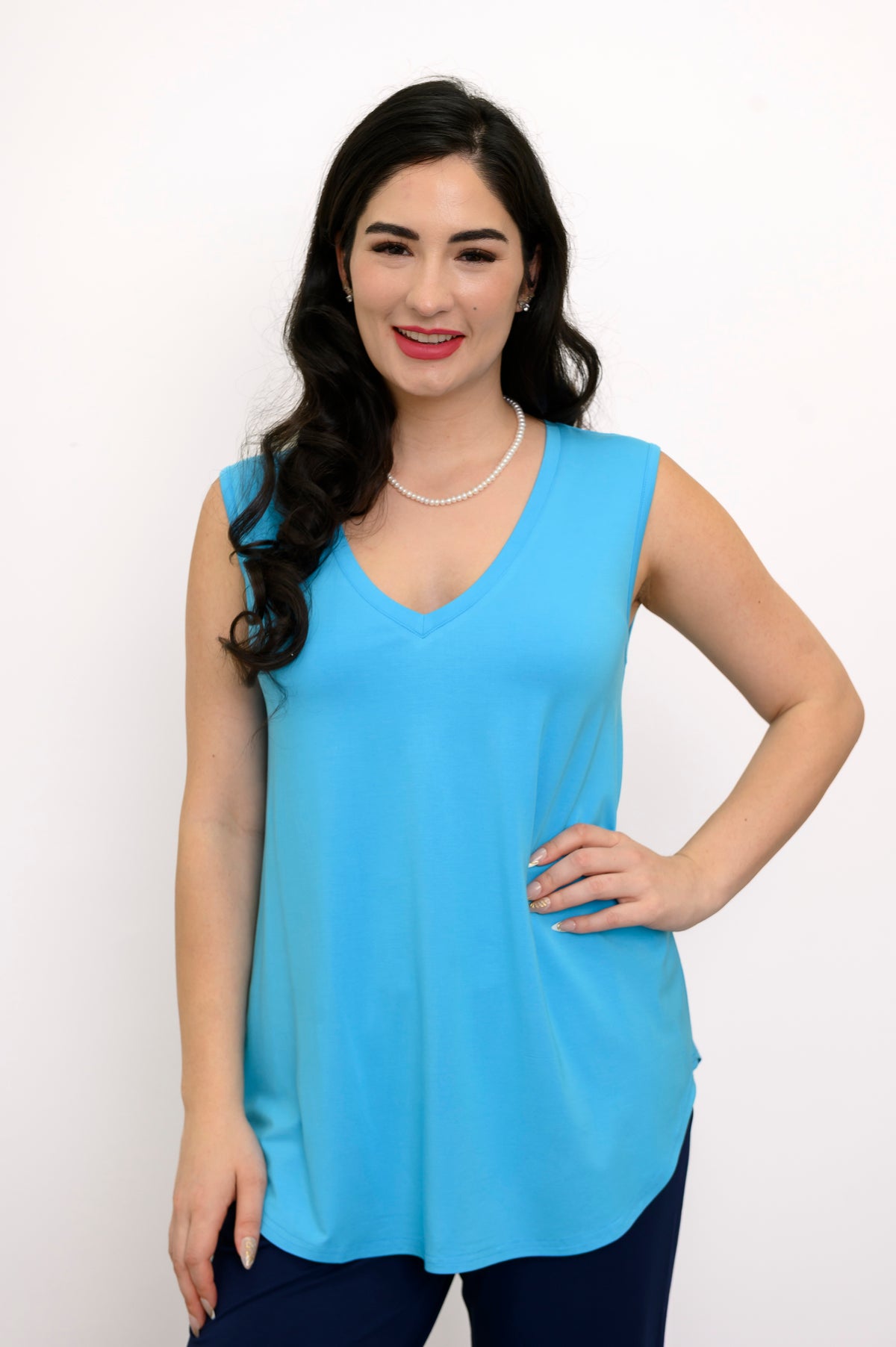 Woman wearing a bright blue sleeveless top and navy pants against a white background, front view