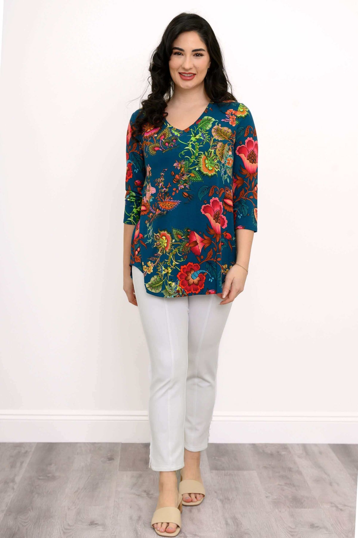Woman in Jackie V Neck bamboo top, teal with bold floral print, front view with white pants