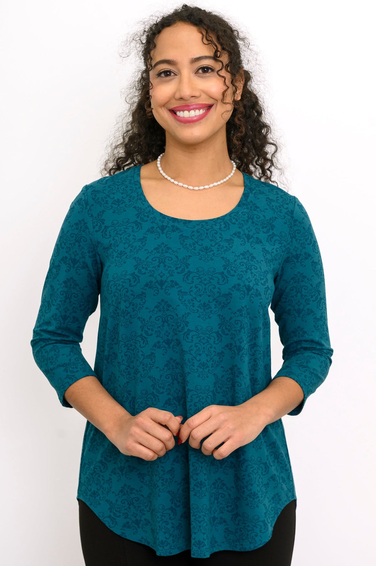A-line patterned teal knit blouse with three-quarter sleeves and a round neckline, styled with black pants.
