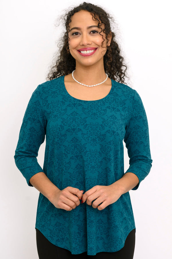 A-line patterned teal knit blouse with three-quarter sleeves and a round neckline, styled with black pants.
