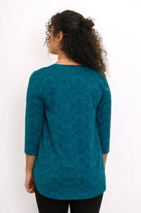 Back view of a teal patterned bamboo top on a model, showcasing its comfortable hip-covering length and fit.