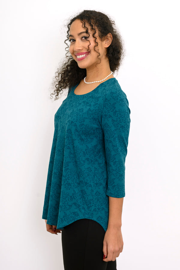 Profile shot of a women's teal geometric print 3/4 sleeve blouse, styled with casual black trousers.