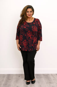 Smiling woman posing in a soft black bamboo-blend top featuring a red botanical print and three-quarter sleeves.