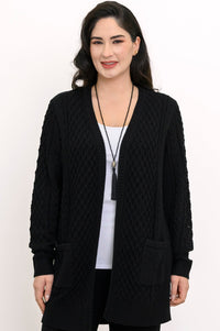 Close up front view of a woman wearing a black cable knit cardigan over a white top and black trousers.